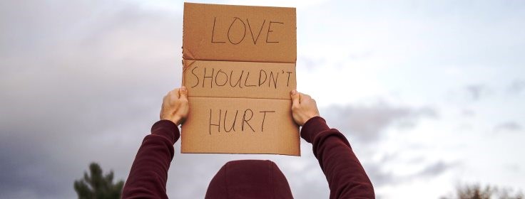 Person with back to camera showing placard with message Love shouldn't hurt